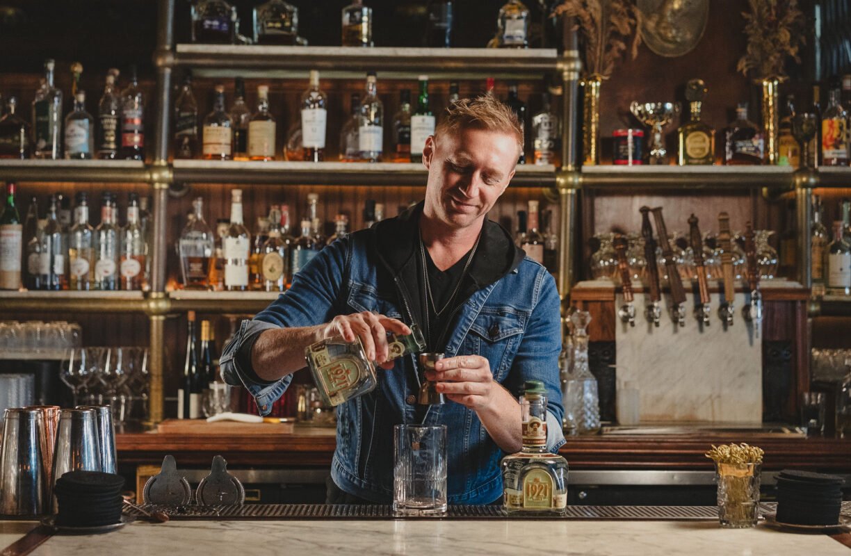 A bartender at The Wolves pours 1921 Blanco behind the bar's backlit wall of bottles.